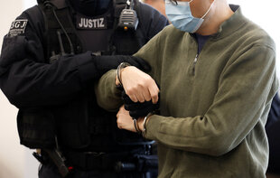 Ein Polizist nimmt einer Person die Handschellen ab, die Gesichter der beiden sind nicht zu sehen