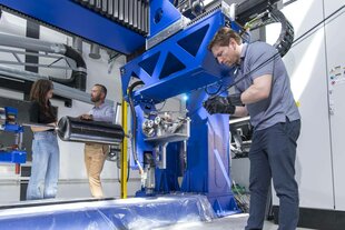 Drei Menschen stehen an einer blauen Maschinenkonstruktion