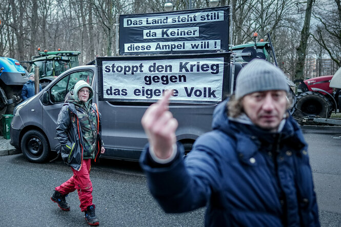 Demonstration von Landwirten. Ein Demonstrant zeigt den Stinkefinger, auf einem LKW steht „stoppt den Krieg gegen das eigene Volk“.
