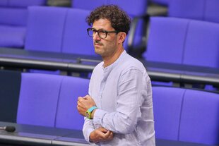 Ein Mann mit Brille fasst sich an seinen linken Ellenbogen
