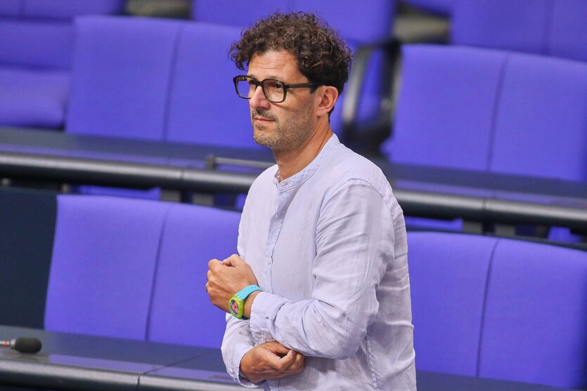 Ein Mann mit Brille fasst sich an seinen linken Ellenbogen