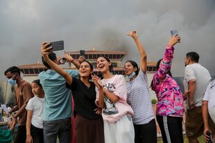 Junge Frauen fotografieren sich vor einem von Rauch verdunkeltem Himmel