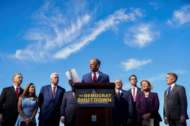 John Thune steht umringt von anderen Republikanern vor einem Stehpult mit der Aufschrift: The Democrat Shutdown