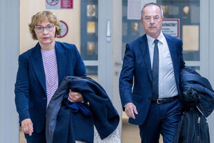 Das Bild zeigt die CDU-Politikerin Susanne Wetterich, die neben ihrem Anwalt Emanuel Burkhardt in den Gerichtssaal des Stuttgart Landgerichts geht. Wetterich ist 69 Jahre alt, sie trägt halblange, dunkelblonde Haare, eine Brille und einen dunklen Hosenanzug, Ihr Antwalt Burkhardt ist etwa 60, er hat einen grauen Schnurrbart, kurzrasierte graue Haare und trägt einen dunkelblauen Anzug. Wetterich trägt in der linken Hand eine weiße Tasche und einen dunkleblauen Mantel, Burkhardt trägt ebenfalls links eine dunkelblaue Daunenjacke und einen schwarzen Rucksack.