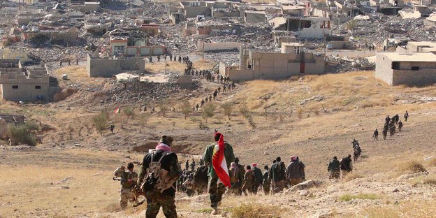 Kurdische Kämpfer gehen einen Berg hinunter in Richtung Stadt