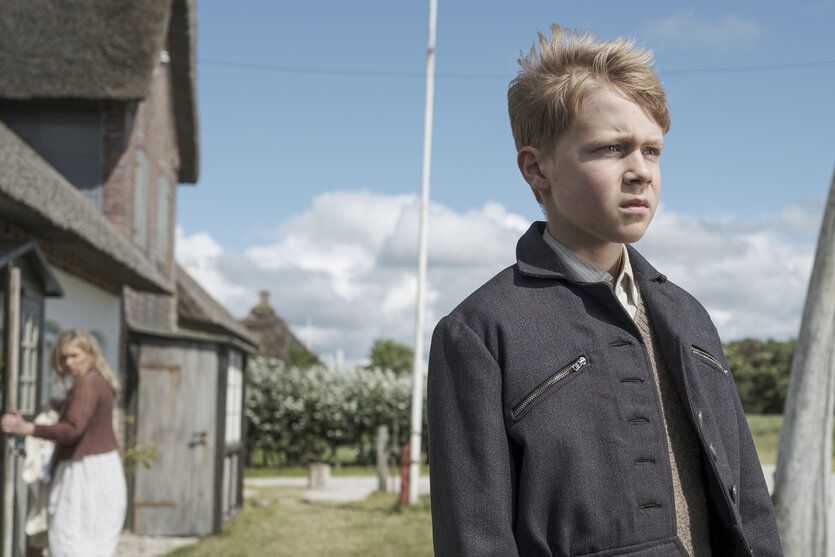 Nanning (Jasper Billerbeck) steht vor dem Haus seiner Eltern, im Hintergrund seine Mutter Hille (Laura Tonke).