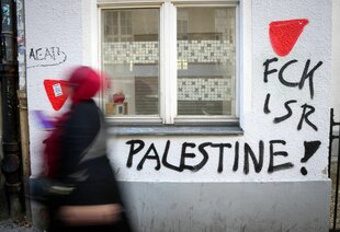Eine Person geht an einer mit Graffity besprühten Hauswand vobei. Dort steht FCK ISR Palestine!