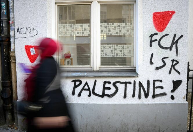 Eine Person geht an einer mit Graffity besprühten Hauswand vobei. Dort steht FCK ISR Palestine!