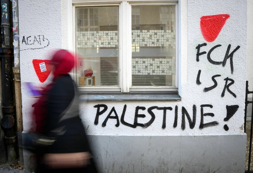 Eine Person geht an einer mit Graffity besprühten Hauswand vobei. Dort steht FCK ISR Palestine!