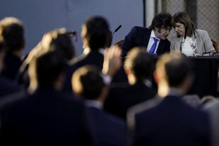 Javier Milei und Patricia Bullrich sitzen auf einer Bühne und stecken die Köpfe zusammen. Im Vordergrund verschwommene Zuschauer*innen.