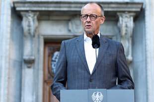 Friedrich Merz steht am Rednerpult an dem der Bundesadler prangt und spricht in ein Mikrofon