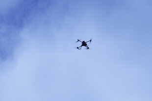 Eine kliene Drohne fliegt - der Himmel ist hellblau - wolkig