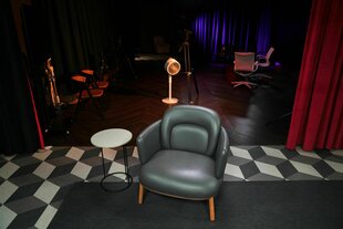Ein leerer grauer Sessel steht auf einem dunklen Teppich in einem Studio - der Boden hat ein Rautenmuster