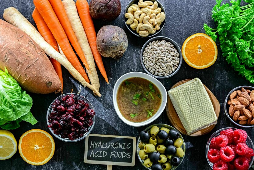 Auf einem Tisch gesundes Essen wie Salat, Süsskartoffeln, Möhren, Pastinaken, rote Beete, Nüsse, Obst, Oliven Kräuter