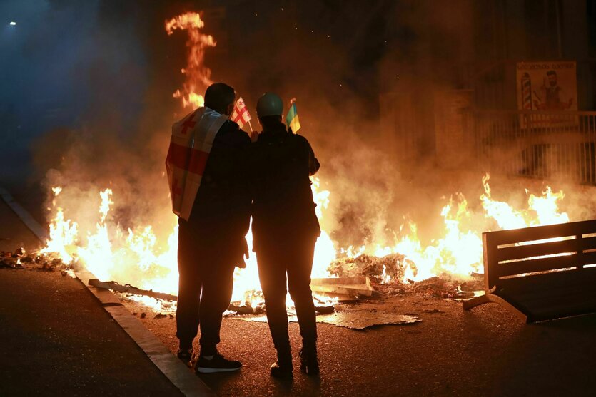 Demonstranten mit einer georgischen und einer ukrainischen Nationalflagge stehen hinter einer brennenden Barrikade unweit einer Polizeiabsperrung