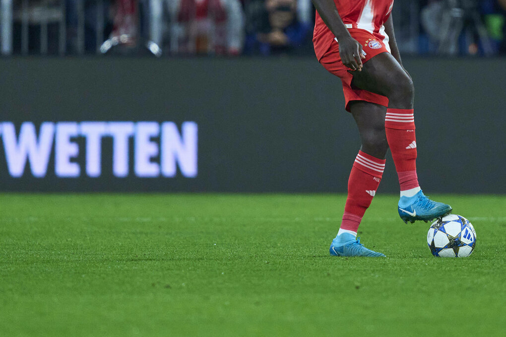 Bandenwerbin "Wetten" hinter einem Bayernspieler mit dem Ball am Fuß