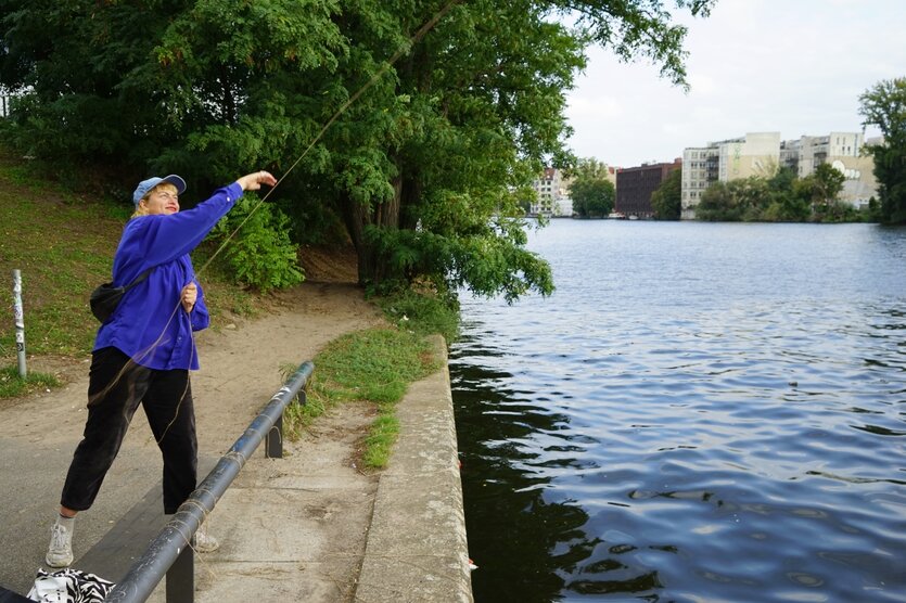 EIne Frau wirft eine Flasche an einer Schnur in die Spree, Teil der Performance "Beton Berlin"