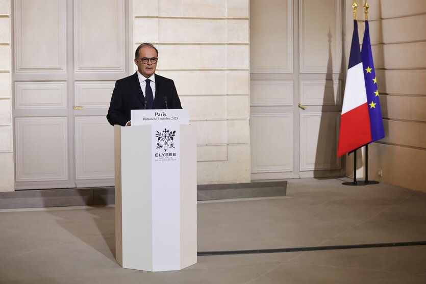 Emmanuel Moulin steht allein an einem weißen Redepult, im Hintergrund eine Frankreich-Fahne