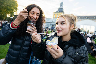 Zwei junge Frauen essen Pudding aus Plastikbechern mit Gabel