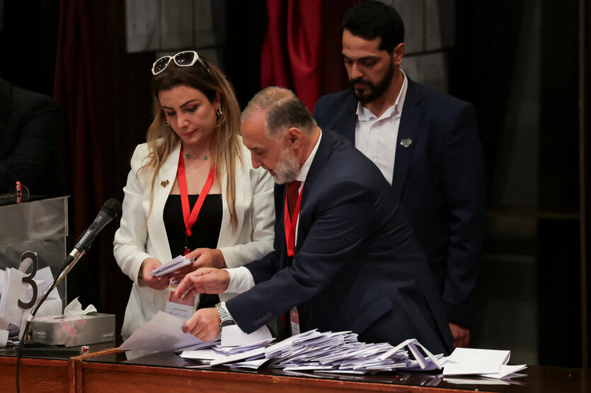 Eine Frau und zwei Männer stehen an einem Tisch mit Zetteln