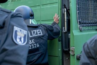 Mehrere Polizisten in voller Montur stehen an einem Polizeitransporter