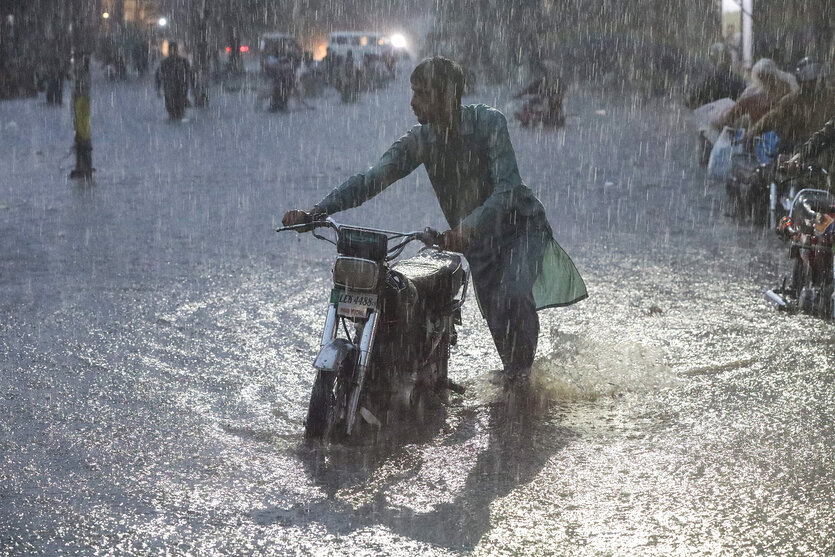 Ein Mann schiebt sein Moped über eine überflutete Straße