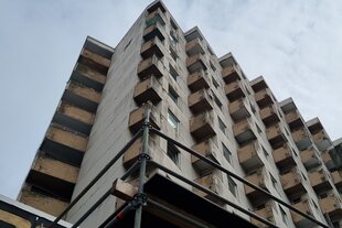 Das Haus am Rembertiring in Bremen von unten fotografiert. Teilweise sind Bruchstellen in der Fassade zu sehen, angeschnitten ist die Ecke eines Baugerüstes, das Fußgänger vor Brocken schützen soll
