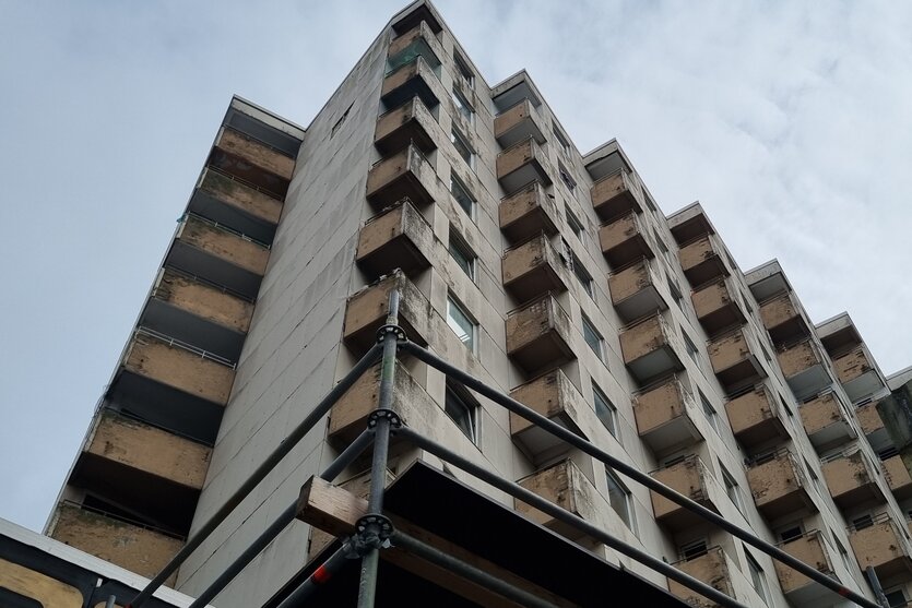 Das Haus am Rembertiring in Bremen von unten fotografiert. Teilweise sind Bruchstellen in der Fassade zu sehen, angeschnitten ist die Ecke eines Baugerüstes, das Fußgänger vor Brocken schützen soll