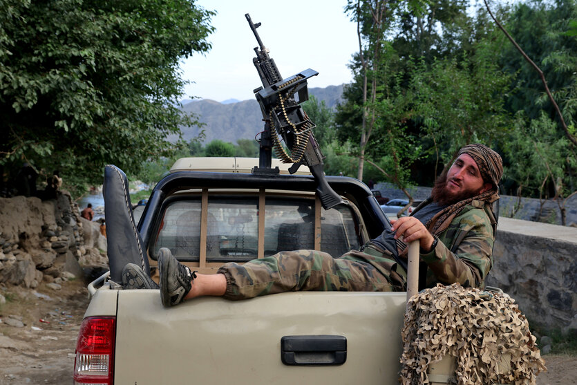 Ein Taliban-Kämpfer sitzt auf der Ladefläche eines Pickups mit aufmontiertem Maschinengewehr, der auf einer steinigen Landstraße steht