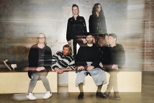Die sechs Musiker der Band Múm sitzen auf flachen Holzbänken.