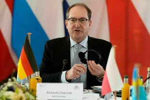 Ein Mann sitzt vor verschiedenen Flaggen und hält einen Kopfhörer in den Händen
