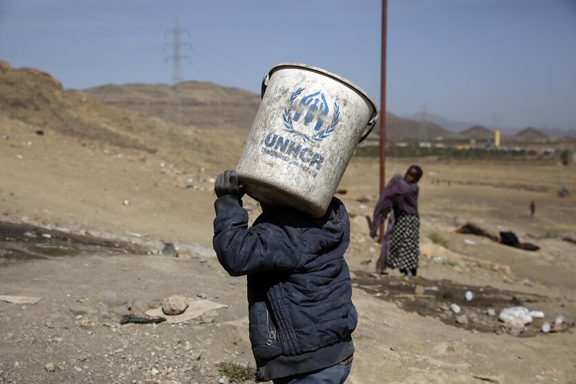 Ein Junge trägt einen Eimer mit dem Logo des Flüchtlingshilfswerks UNHCR