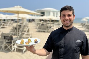 Ein Mann steht an einem Strand und hält einen Teller mit einem Olivengericht in der Hand