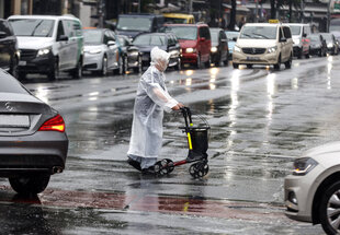 Mensch mit Rollator überquert Straße bei Regen