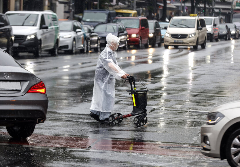 Mensch mit Rollator überquert Straße bei Regen