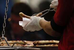 Die Hand eines Wurstverkäufers hält eine Bratwurst an einem Bratwurtsstand