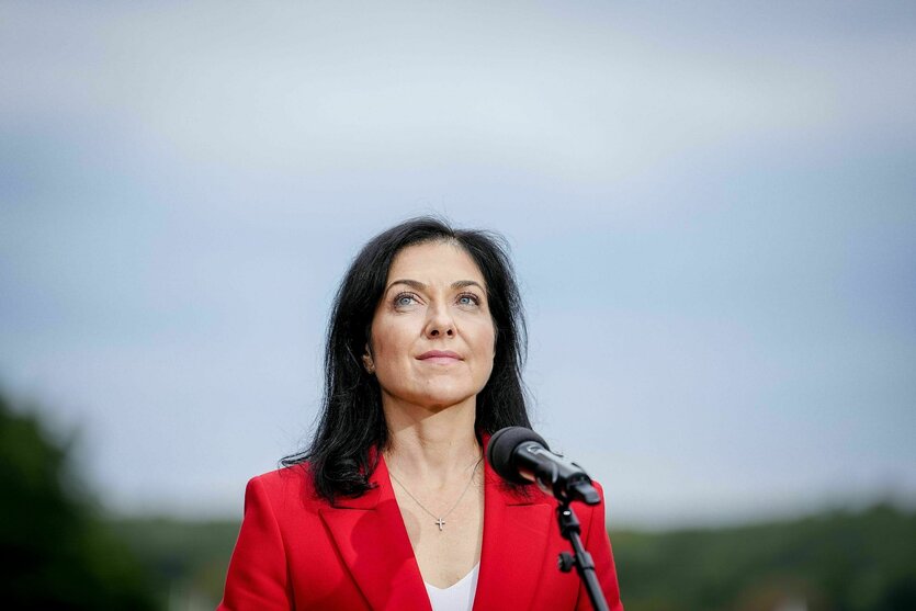 Katherina Reiche steht unter blauem Himmel vor einem Mikrofon und blickt nach oben