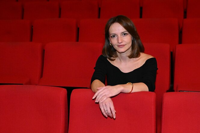 Eine junge Frau sitzt allein auf roten Theaterstühlen