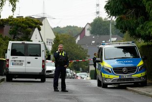 Ein Polizist steht neben einem Polizeiwagen auf einer Straße in einem Wohnviertel