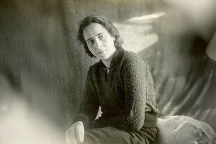 Hannah Arendt sitzt vor einer mit Stoff behangenen Wand.