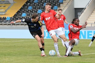 Männer in Fußballtrikots kämpfen um den Ball auf dem Rasen