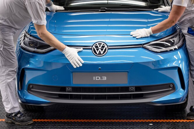 Zwei Arbeiter prüfen den Lack eines VWs, sie tragen weiße Handschuhe