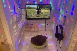 In einem Kühlschrank befindet sich auf einem grünen Servierteller ein Kuhfladen. Darüber ist ein Bildschirm installiert mit einem Erklärvideo. Der Kühlschrank ist von Disco-Lichtern beleuchtet.
