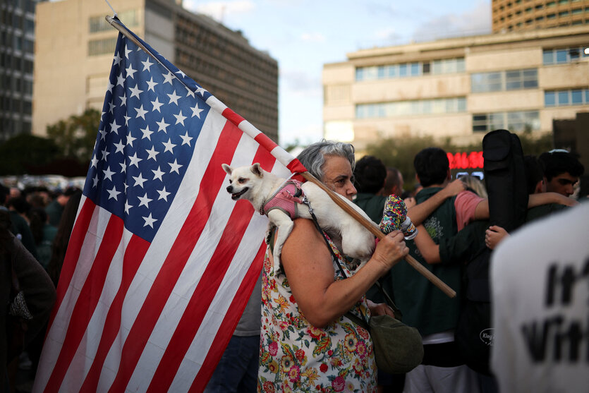 Eine frau trägt einen kleinen Hund und die Stange einer US Flagge über der rechten Schulter