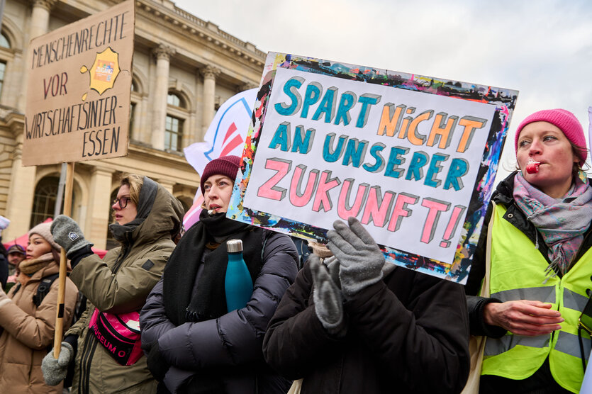 Demonstrierende mit Trillerpfeifen in Berlin, eine trägt ein Schild mit der Aufschrift "Spart nicht an unserer Zukunft"