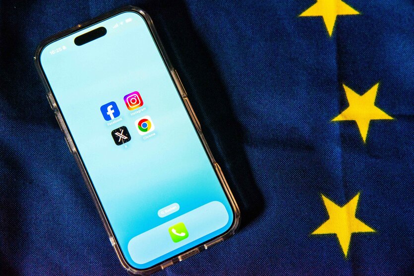 Die Logos von Facebook, Instagram, X (ehemals Twitter) und Google Chrome sind auf dem Bildschirm eines Smartphones zu sehen, das auf einer EU-Flagge liegt