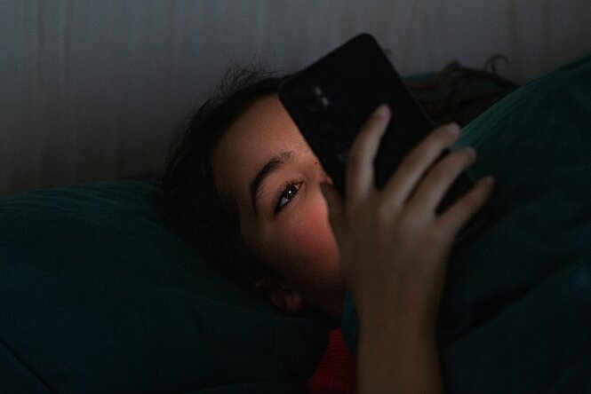 Eine Jugendliche liegt im Bett und schaut auf das Display ihres Smartphones