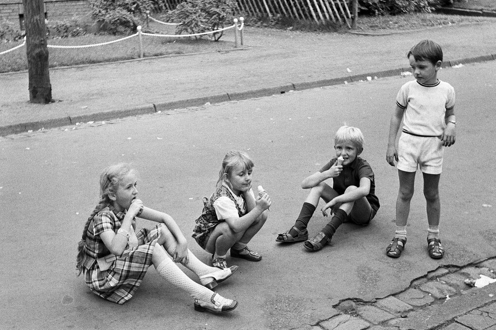 Historische Schwarz-weiß-Aufnahme von Kindern, die auf dem Straßenpflaster sitzen und Eis essen