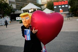 Eine Frau mit Trump-Maske hält einen Luftballon in Herzform in den Händen