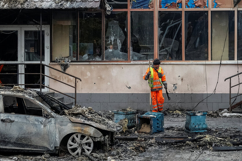 Ein Mann in orangefarbener Arbeitskleidung steht vor einem zerstörten Haus